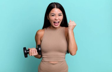 İspanyol güzel kadın şokta, gülüyor ve başarıyı kutluyor. Fitness konsepti ve dambıl