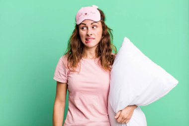 hispanic pretty woman looking puzzled and confused wearing pajamas and a pillow