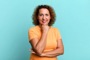 Orta yaşlı İspanyol kadın mutlu görünüyor ve gülümsüyor. Çenesi açık, merak ediyor ya da soru soruyor. Seçenekleri karşılaştırıyor.