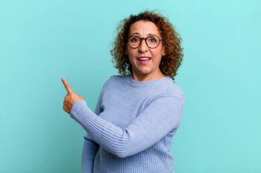 Orta yaşlı İspanyol bir kadın heyecanlı ve şaşırmış görünüyor. Yana ve yukarıya bakıp boşluğu kopyalıyor.