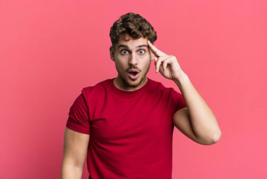 young adult caucasian man looking surprised, open-mouthed, shocked, realizing a new thought, idea or concept