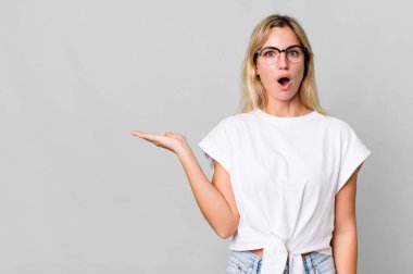 caucasian blonde woman looking surprised and shocked, with jaw dropped holding an object. copy space concept