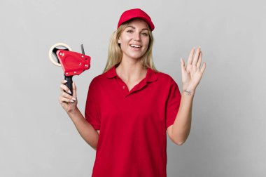 caucasian blonde woman smiling happily, waving hand, welcoming and greeting you. shipping packer concept