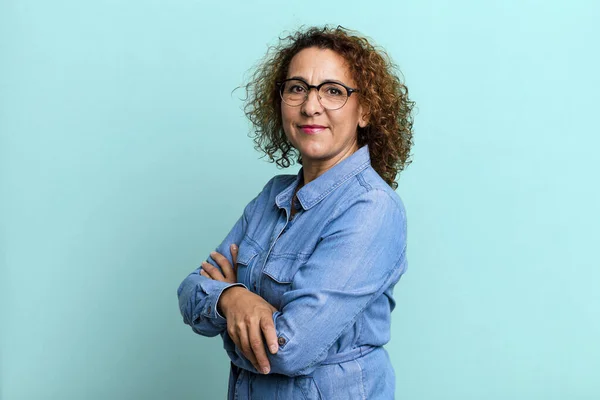 middle age hispanic woman smiling to camera with crossed arms and a happy, confident, satisfied expression, lateral view