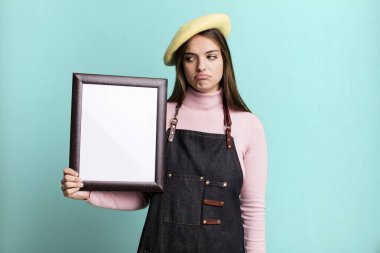 young pretty woman feeling sad, upset or angry and looking to the side. empty picture frame concept