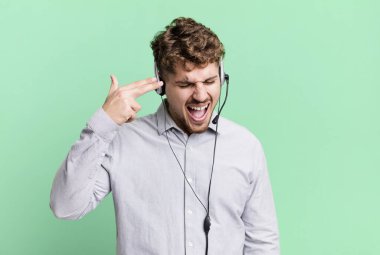 young adult caucasian man looking unhappy and stressed, suicide gesture making gun sign. telemarketer agent concept