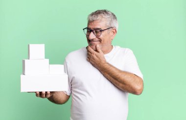 Orta yaşlı bir adam mutlu, kendinden emin ve elleri çenesinde gülümsüyor. farklı paketler boş kutular