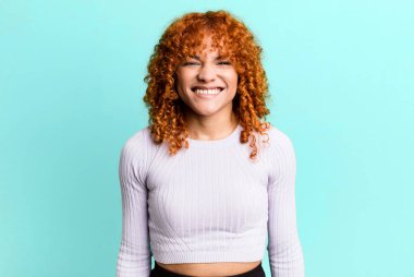 Kızıl saçlı, güzel bir kadın mutlu ve şapşal görünüyor. Geniş, eğlenceli, kaçık bir gülüşü ve açık gözlü.