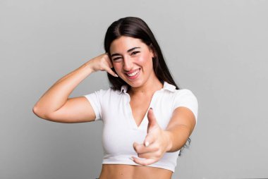 Neşeli bir şekilde gülümsüyor ve telefonla konuşurken kamerayı işaret ediyor.