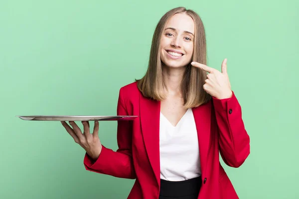 smiling confidently pointing to own broad smile. businesswoman presenting with a tray