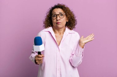 pretty middle age woman feeling puzzled and confused and doubting. tv presenter with a microphone concept