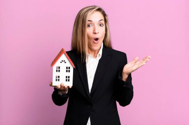 pretty blonde woman looking surprised and shocked, with jaw dropped holding an object. real state concept