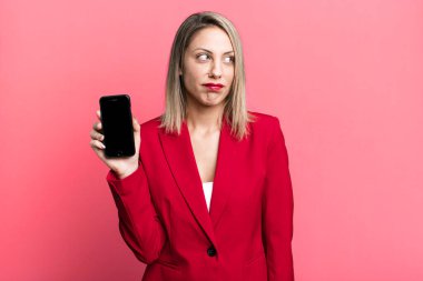 pretty blonde woman feeling sad, upset or angry and looking to the side. businesswoman showing a phone screen
