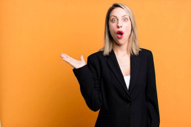 pretty blonde woman looking surprised and shocked, with jaw dropped holding an object. businesswoman concept