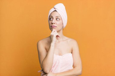 pretty blonde woman thinking, feeling doubtful and confused. bathrobe and beauty concept