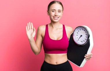 caucasian pretty woman smiling happily, waving hand, welcoming and greeting you. fitness and diet concept