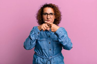 Orta yaşlı Latin bir kadın ciddi görünüyor ve iki parmağının önde olmasını istemiyor. Sessizlik istiyor.