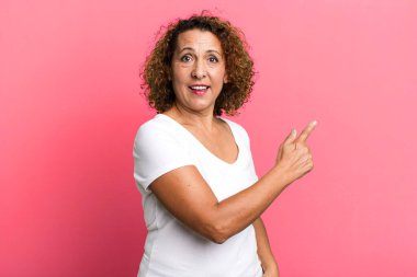 Orta yaşlı İspanyol bir kadın heyecanlı ve şaşırmış görünüyor. Yana ve yukarıya bakıp boşluğu kopyalıyor.