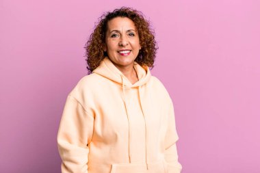 Orta yaşlı İspanyol kadın neşeli, mutlu, kendinden emin ve rahat bir ifadeyle gülümsüyor.