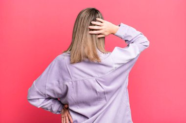 blonde adult woman thinking or doubting, scratching head, feeling puzzled and confused, back or rear view