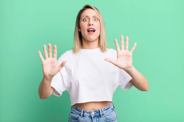 blonde adult woman feeling stupefied and scared, fearing something frightening, with hands open up front saying stay away