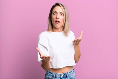 blonde adult woman feeling extremely shocked and surprised, anxious and panicking, with a stressed and horrified look