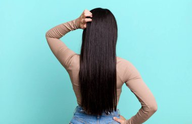 Güzel Latin bir kadın bilgisiz ve kafası karışık, bir çözüm düşünüyor, eli kalçasında, diğeri kafasında, dikiz aynasından.