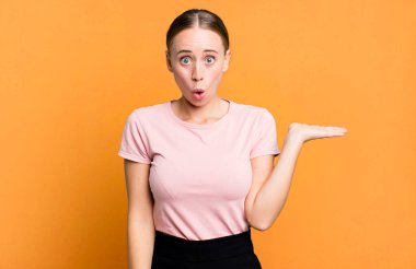 Şaşırmış ve şoke olmuş bir halde, çenesi düşmüş bir objeyi elinde açık bir elle tutarken.