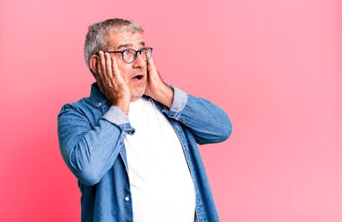 Orta yaşlı bir adam mutlu, heyecanlı ve şaşırmış hissediyor. İki eli yüzü de havada bir tarafa bakıyor.