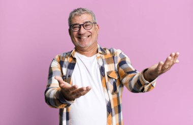 Orta yaşlı bir adam neşeli bir şekilde gülümsüyor. Sıcak, dostça, sevgi dolu bir kucaklama yapıyor. Mutlu ve sevimli hissediyor.