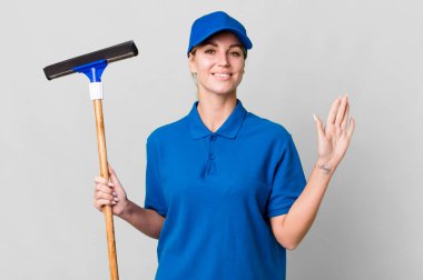 caucasian blonde woman smiling happily, waving hand, welcoming and greeting you. windows washer concept
