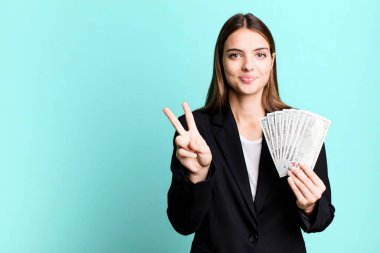 Gülümseyen ve mutlu görünen genç, güzel bir kadın zafer ya da huzur simgesi. iş ve dolar banknotları kavramı