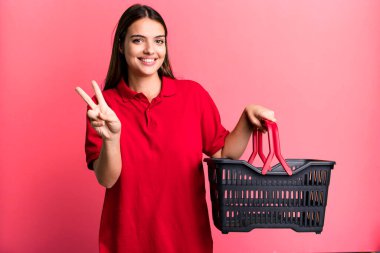 Gülümseyen ve mutlu görünen genç, güzel bir kadın zafer ya da huzur simgesi. boş alışveriş sepeti kavramı