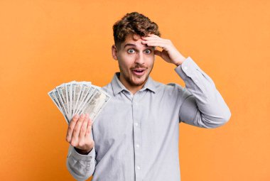 young adult caucasian man looking happy, astonished and surprised. dollar bank notes concept