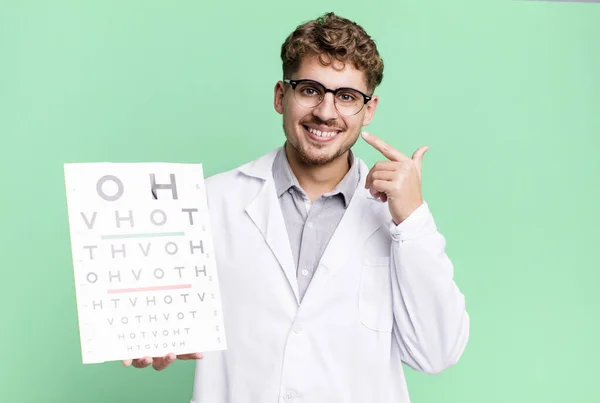young adult caucasian man smiling confidently pointing to own broad smile. optical vision test concept