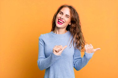 Genç ve güzel bir kadın neşeyle gülümsüyor ve yan taraftaki fotokopi alanını işaret ediyor, mutlu ve tatmin olmuş hissediyor.