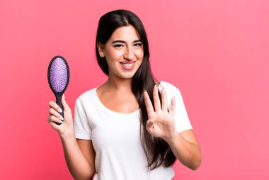 smiling and looking friendly, showing number four. hair comb concept