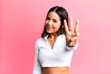 İspanyol güzel kadın gülümsüyor ve arkadaş canlısı görünüyor. Üç ya da üç numarayı gösteriyor. Elleri önde, geriye doğru sayıyor.