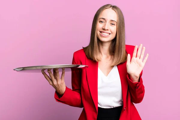 smiling happily, waving hand, welcoming and greeting you. businesswoman presenting with a tray