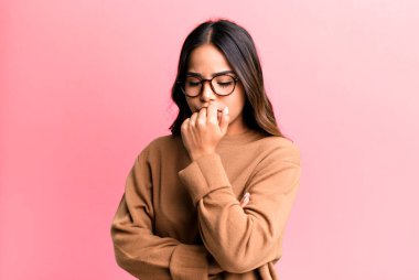 Hispanik güzel kadın ciddi, düşünceli ve endişeli, elleri çenesine bastırılmış şekilde yan bakıyor