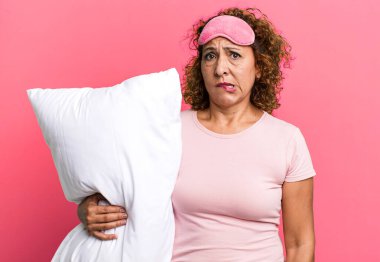 pretty middle age woman looking puzzled and confused wearing pajamas night wear and a pillow