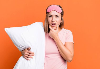 pretty blonde woman with mouth and eyes wide open and hand on chin. pajamas or nightwear concept