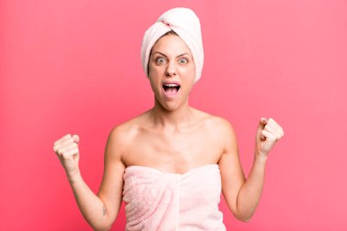pretty blonde woman shouting aggressively with an angry expression. bathrobe and beauty concept