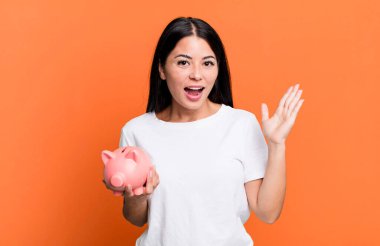 hispanic pretty woman feeling happy, surprised realizing a solution or idea with a piggy bank