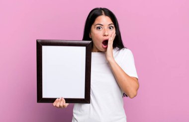 Hispanik güzel kadın boş bir çerçeve ile şok ve korkmuş hissediyor