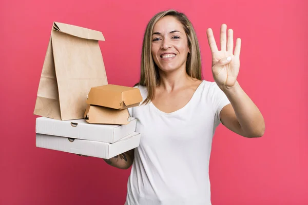 かなりブロンドの女性は笑顔で友好的に見える4番目を示してる 配送は食品パッケージの概念を取り除き — ストック写真