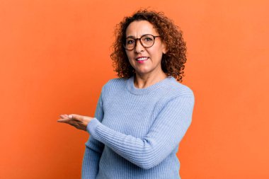 Orta yaşlı İspanyol kadın neşeli bir şekilde gülümsüyor, mutlu hissediyor ve fotokopi alanında bir kavram gösteriyor.