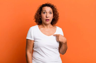 Orta yaşlı, şaşkın ve şaşkın görünen, ağzı açık, kendini işaret eden İspanyol bir kadın.