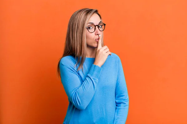 blonde adult woman asking for silence and quiet, gesturing with finger in front of mouth, saying shh or keeping a secret