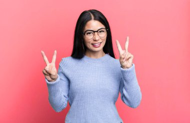 Güzel Latin kadın gülümsüyor ve mutlu görünüyor, arkadaş canlısı ve memnun, zafer ya da barış işareti yapıyor iki elinle